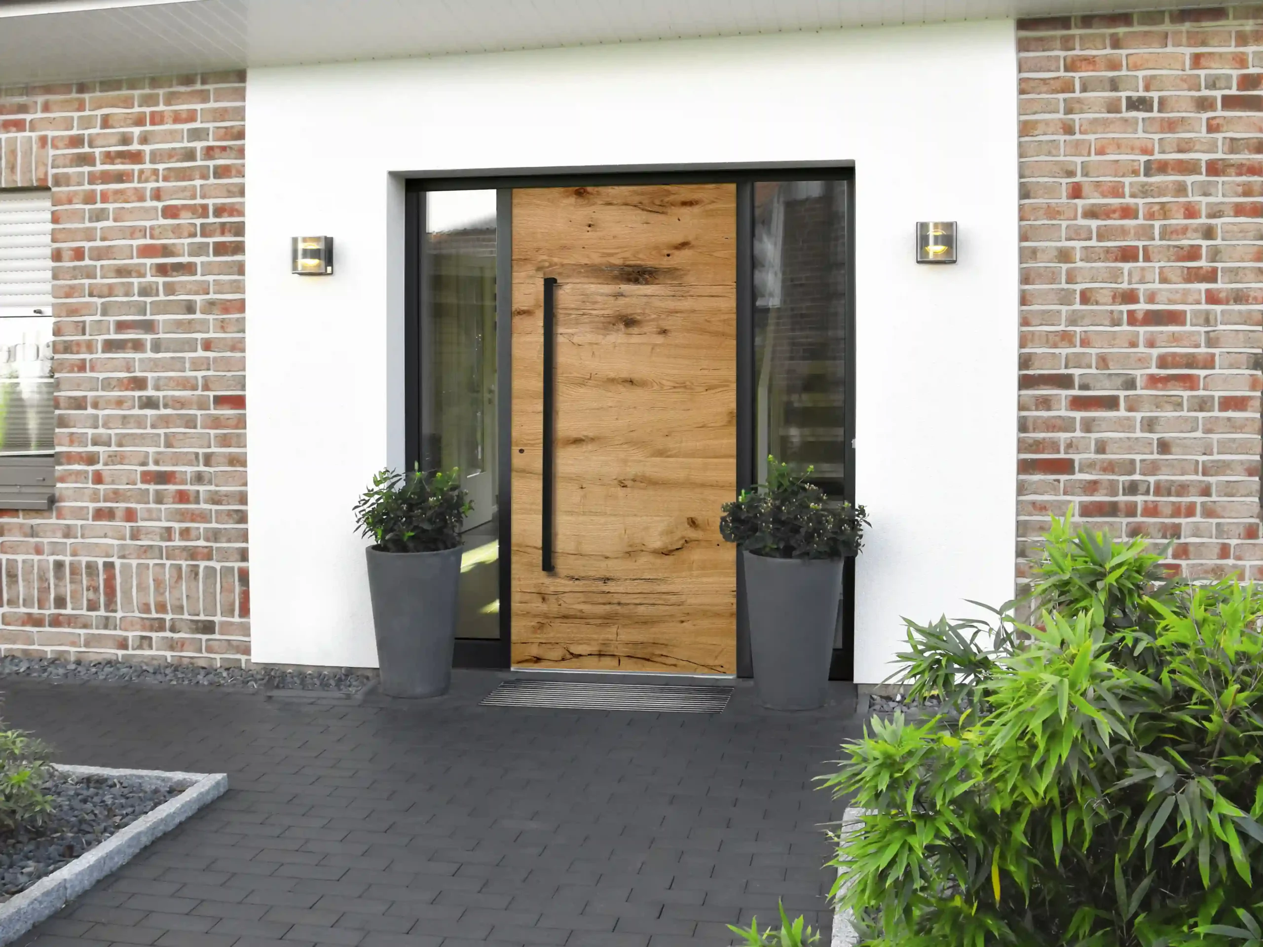 Stilvolle Außenterrasse mit Lamellendach und Beleuchtung Hölzerne Haustür mit beidseitigen Glaselementen an modernem Backsteinhaus.
